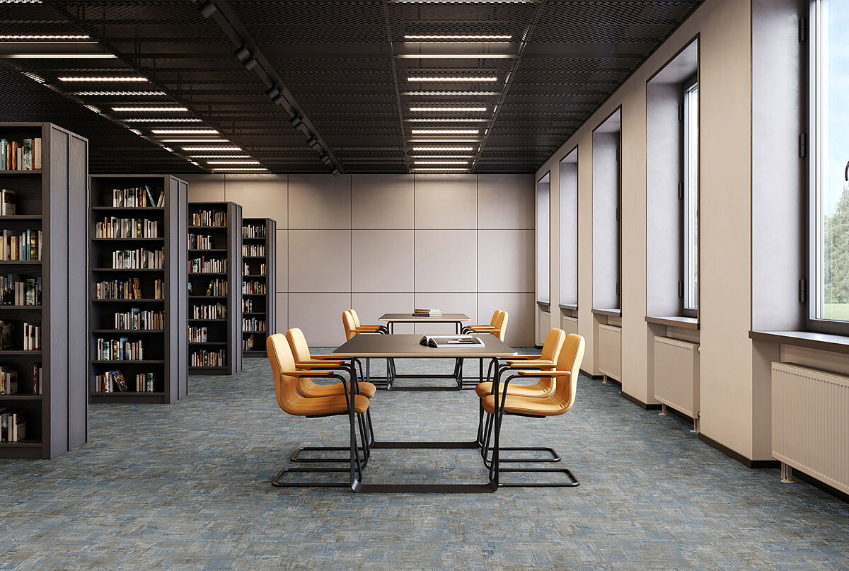 Reading room with bookshelves, tables and yellow chairs on recycled elastic flooring in a blue-grey mottled tile look.