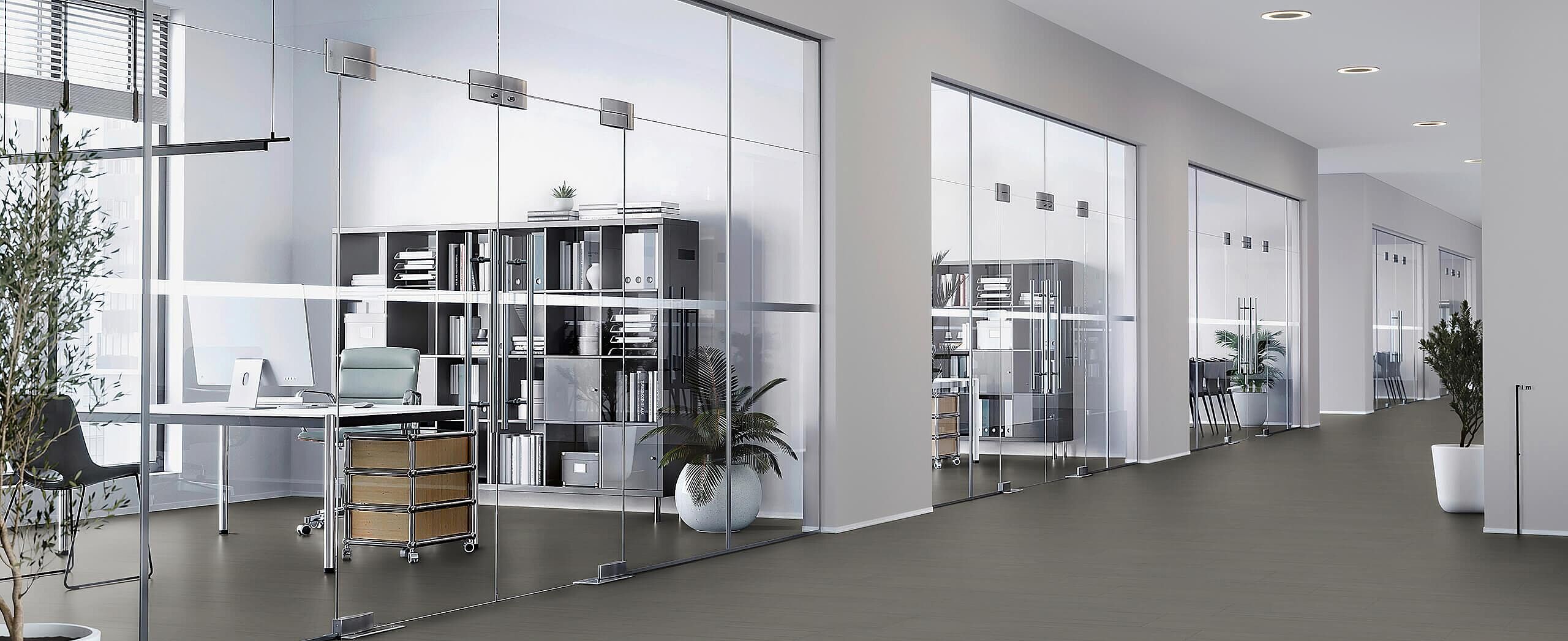 Modern office with glass walls and workstations, recycled elastic flooring in a dark grey finish with a calm matte surface.